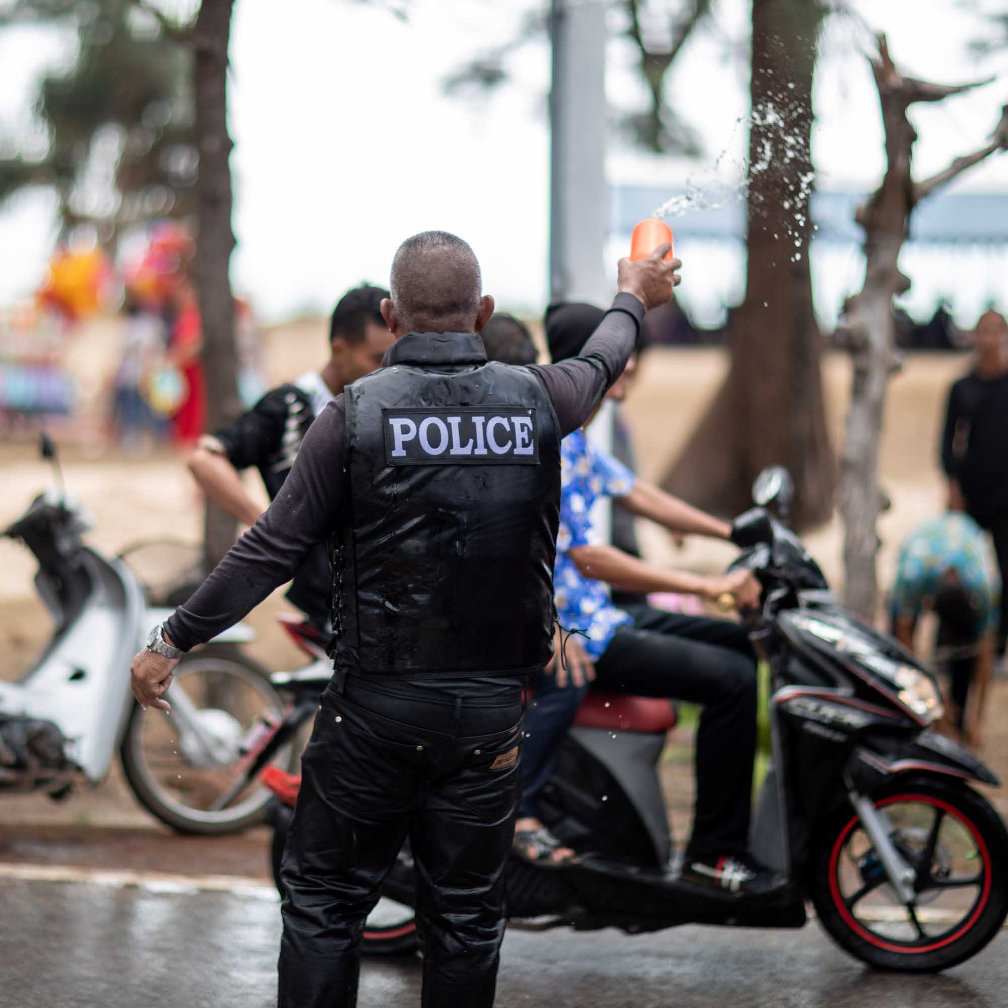 Police officer throws water at boys on motorbike during Songkran water festival in Phuket, Thailand | Street Photography | Travel Photography | Festival Photography