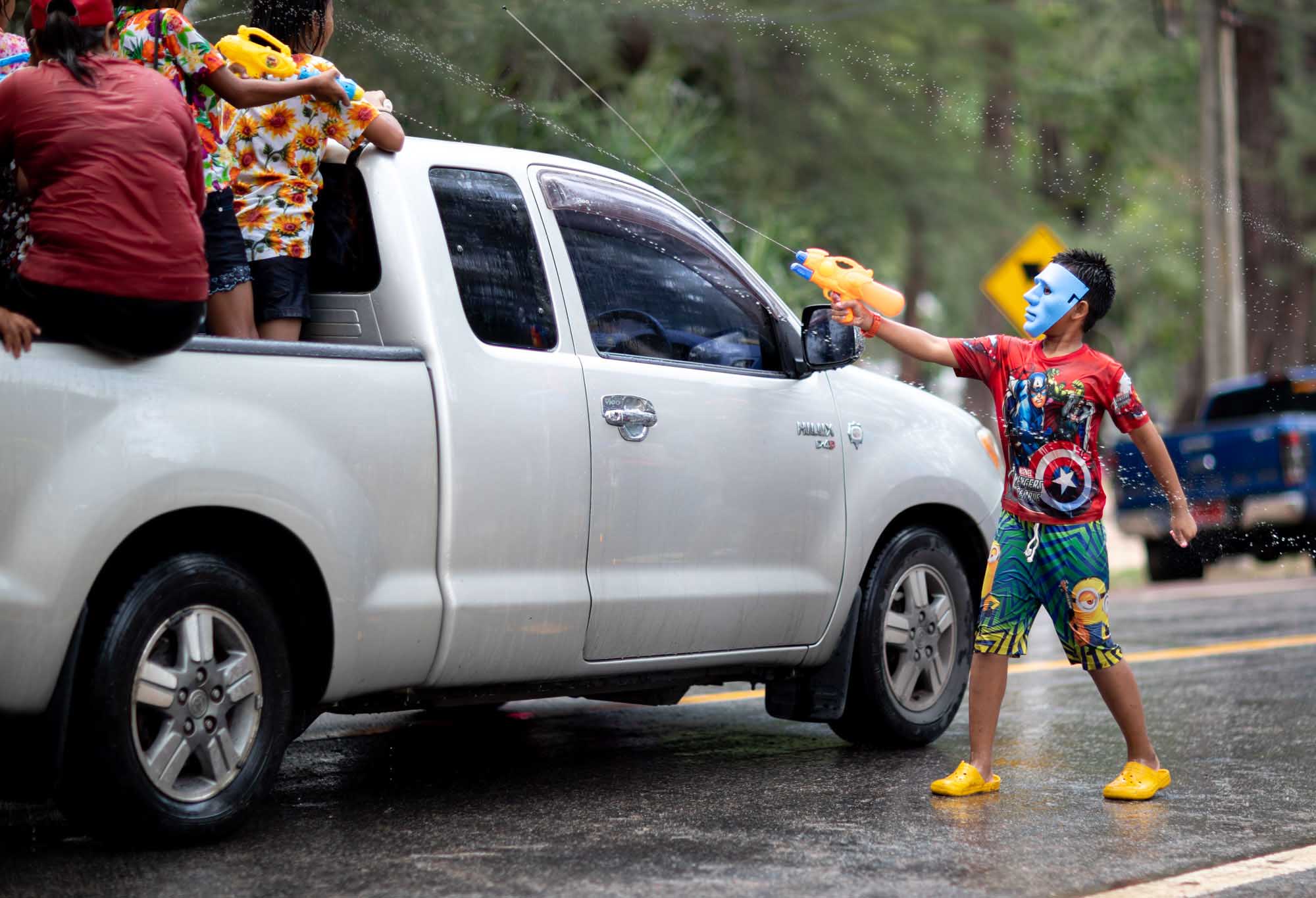 Boy with mask squirts water at truck during Songkran water festival in Phuket, Thailand | Street Photography | Travel Photography | Festival Photography