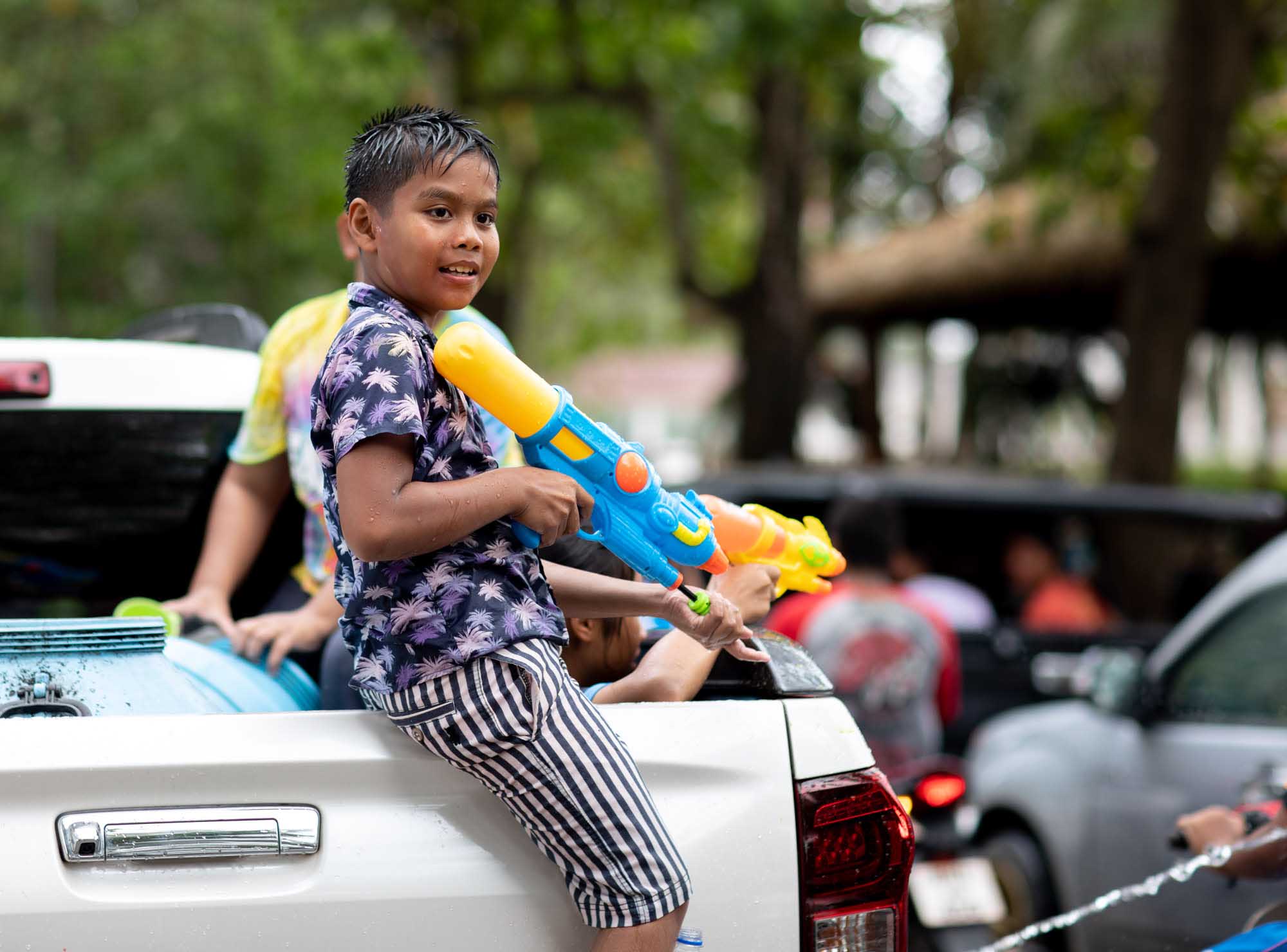 Boy sits on back of truck with squirt gun during Songkran water festival in Phuket, Thailand