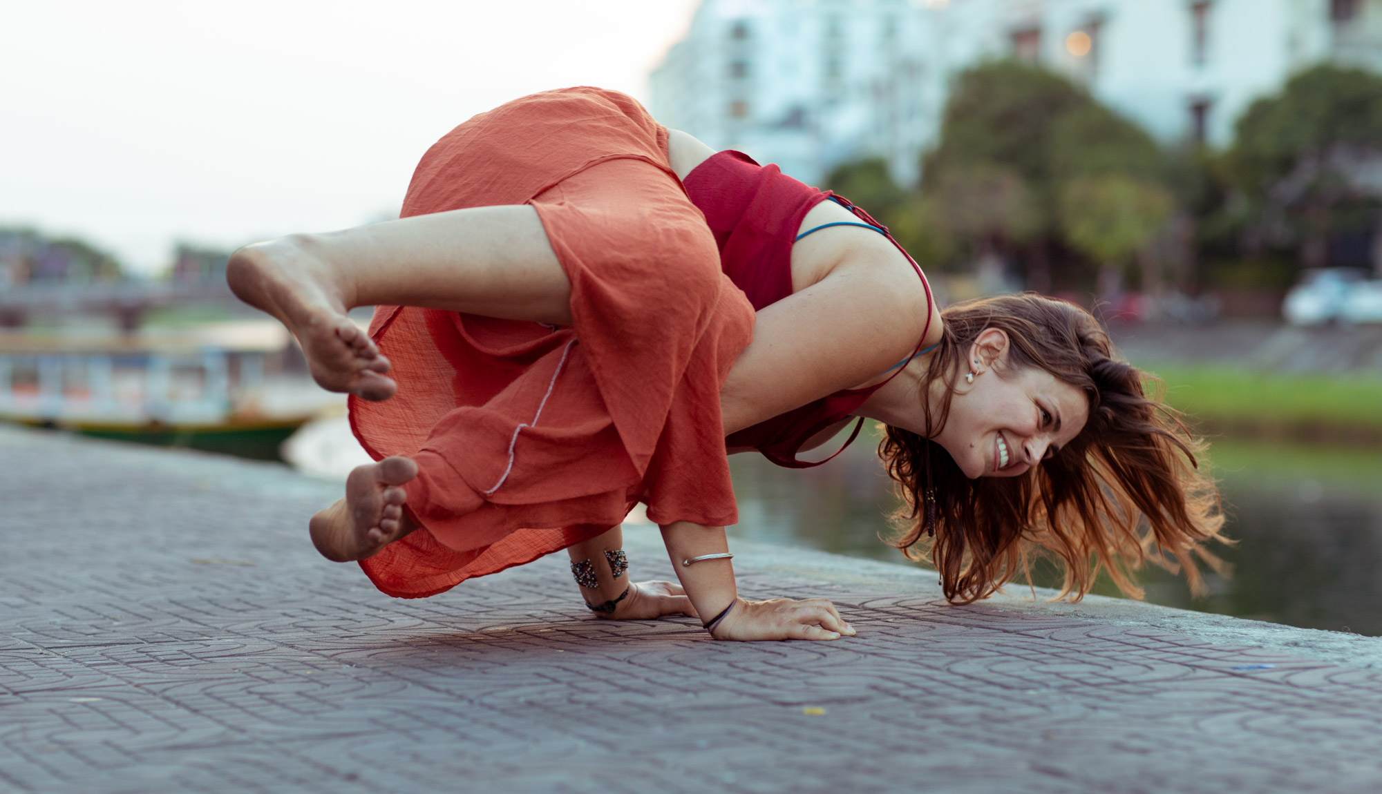 Woman laughs while attempting a yoga pose near a river