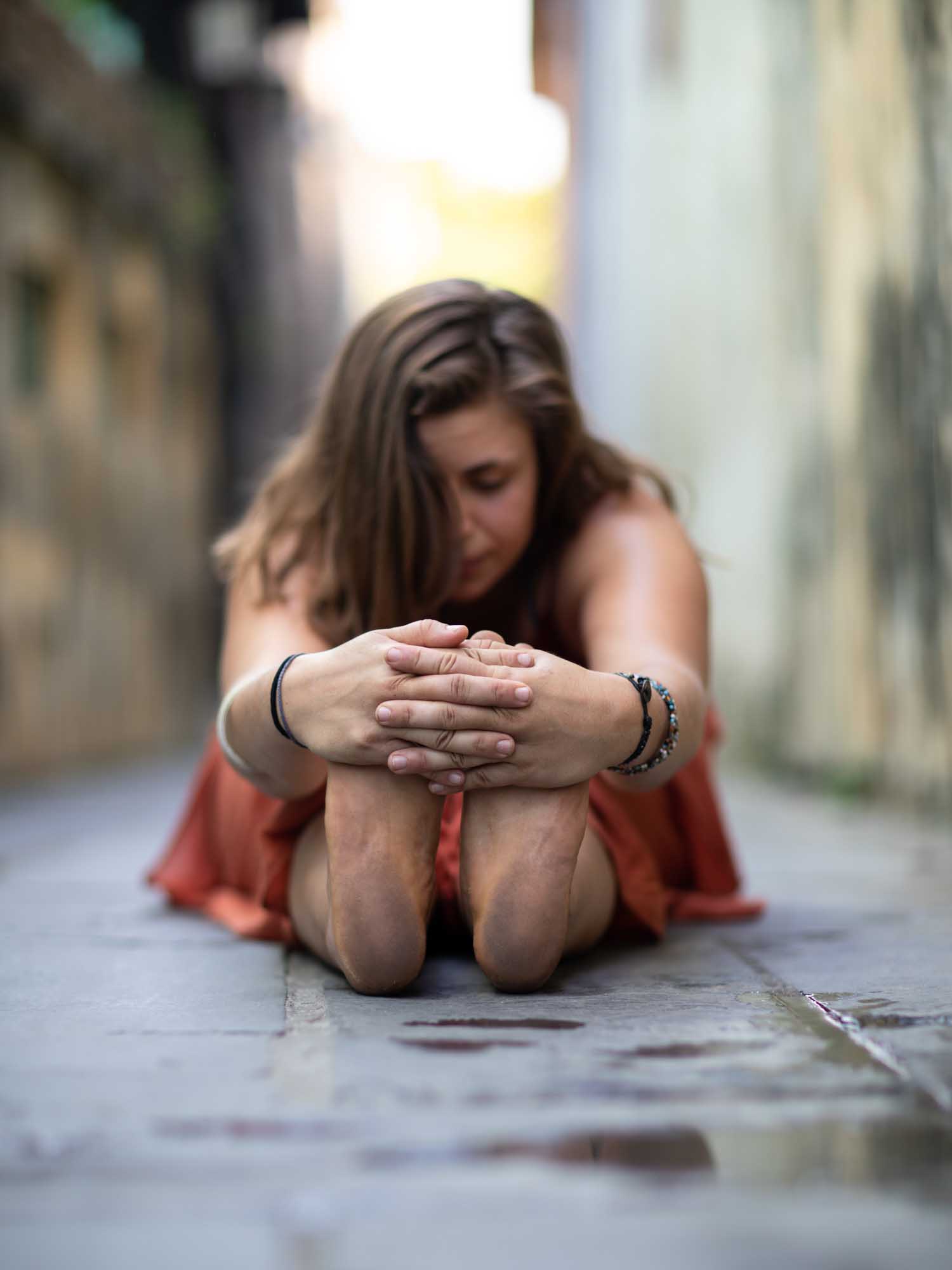Woman touches her toes in a sitting position in an alleyway