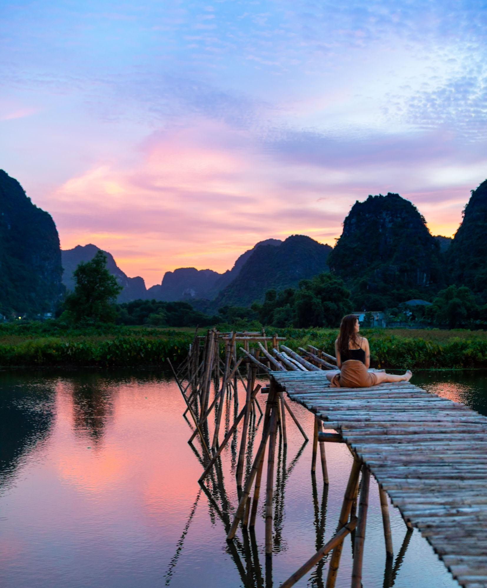 Woman watches colorful sunset on bridge over lake in Trang An, Vietnam | Travel Photography